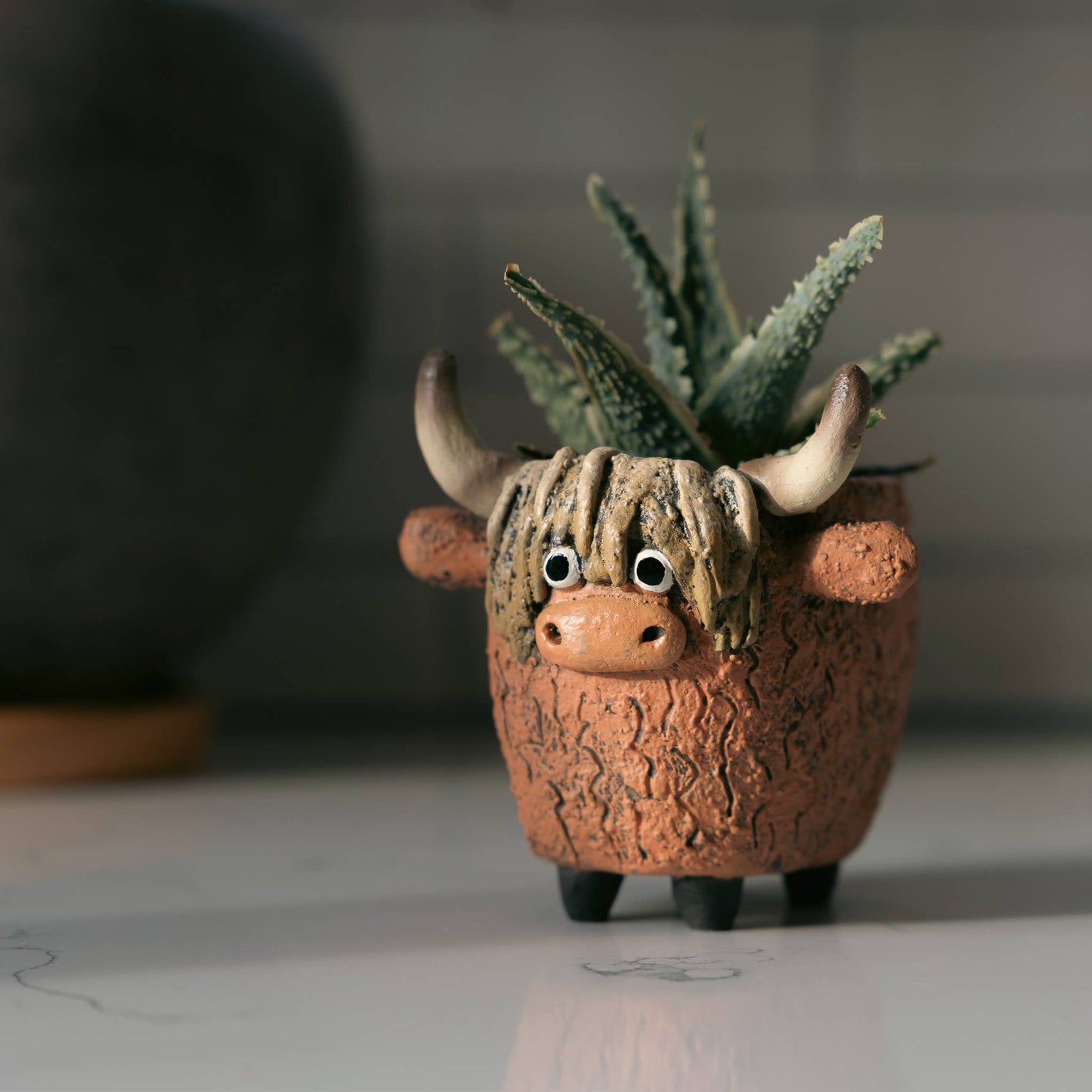 Ceramic planter shaped like a highland cow with a small succulent inside, on a neutral background.