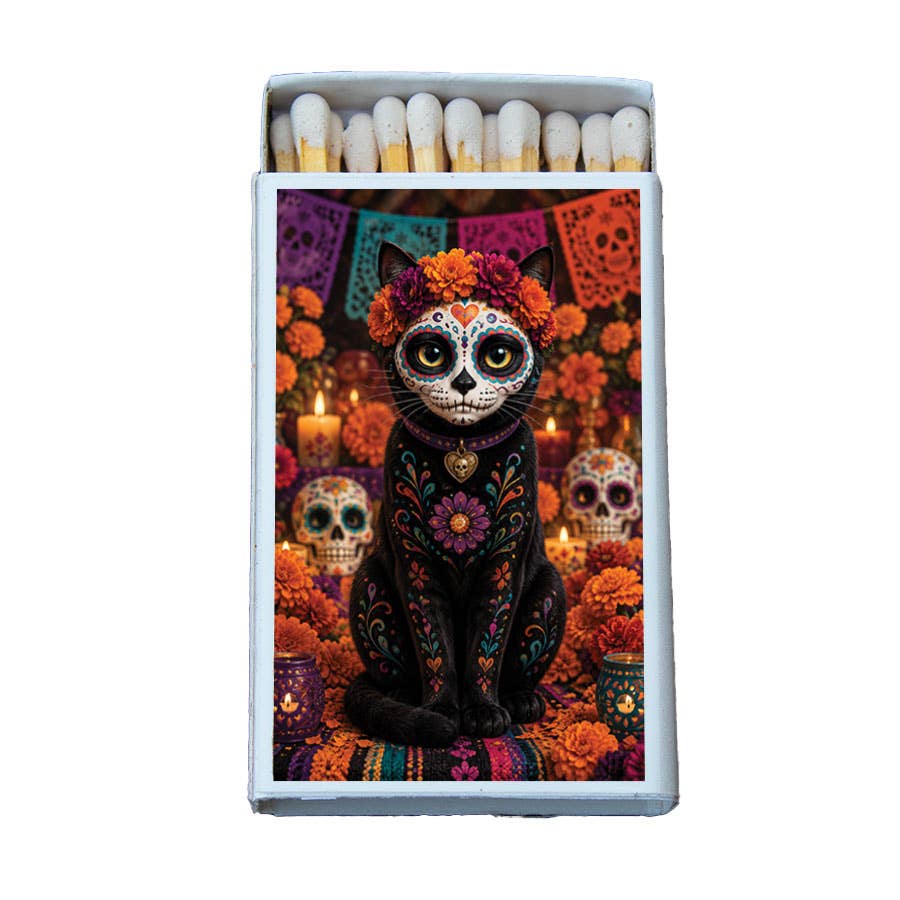 A matchbox with a colorful Day of the Dead cat illustration on the front, shown open with white matches inside against a plain white background.