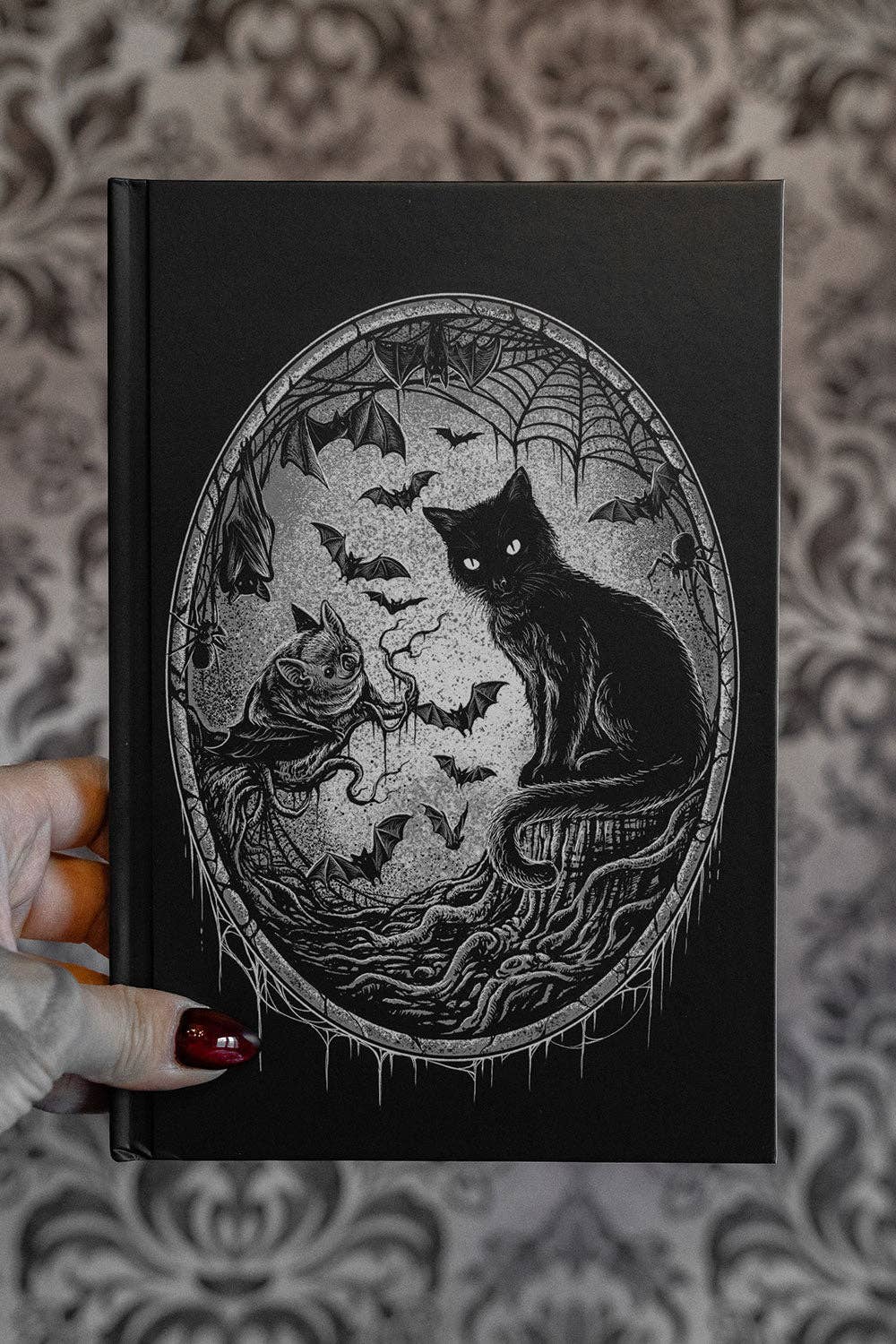 Black journal with a black cat illustration held by a hand against a patterned background