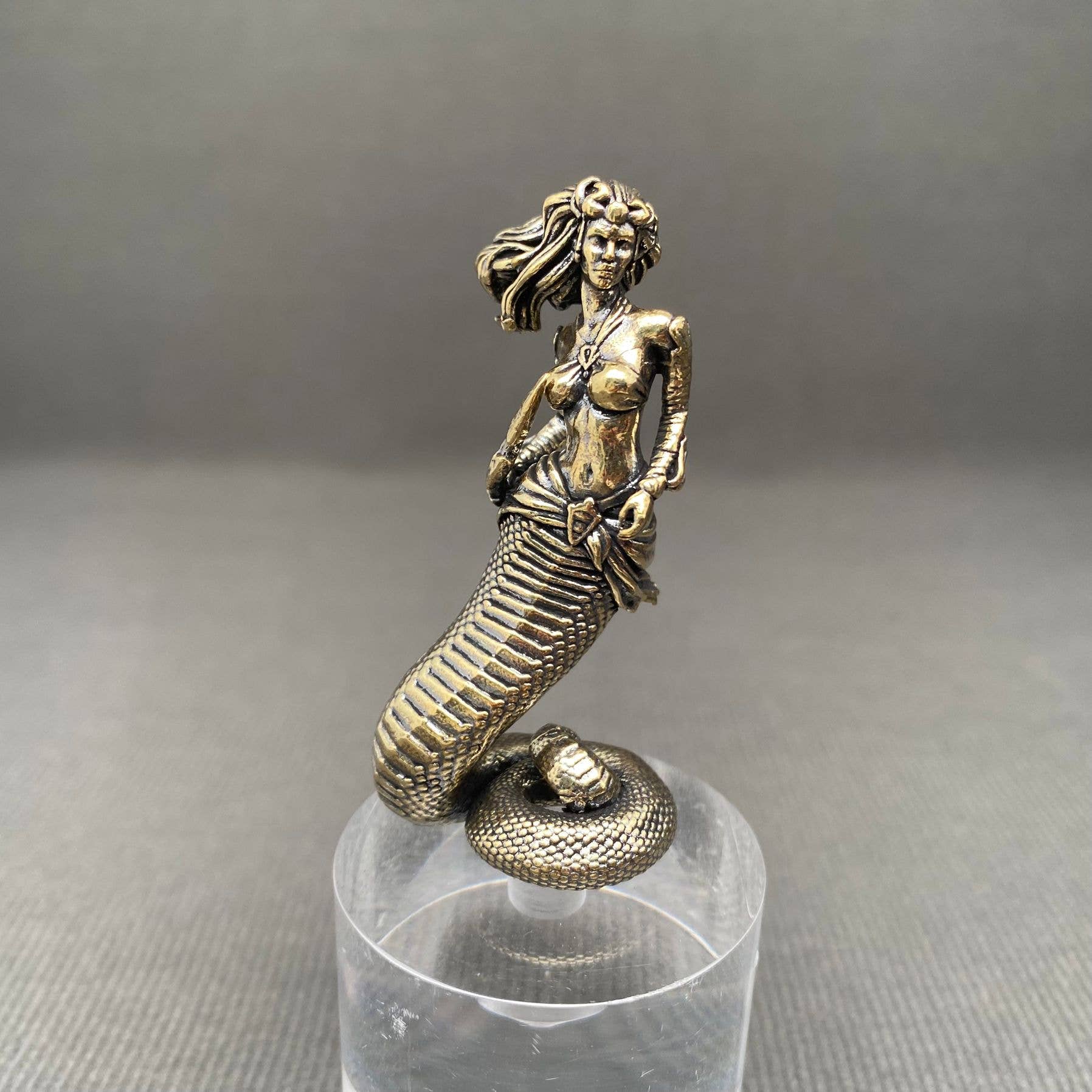 Bronze Medusa figurine on a clear stand against a gray background