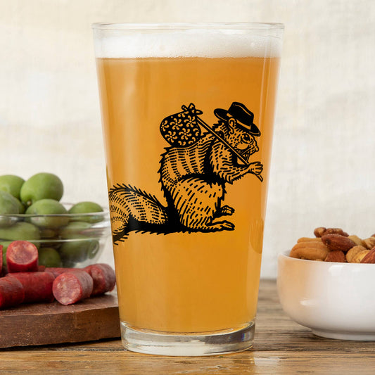Pint glass with a squirrel design filled with beverage, placed on a wooden surface with snacks.