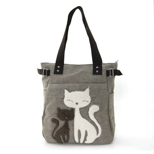 A grey tote bag with cat motifs, featuring faux fur and studs, with black handles.