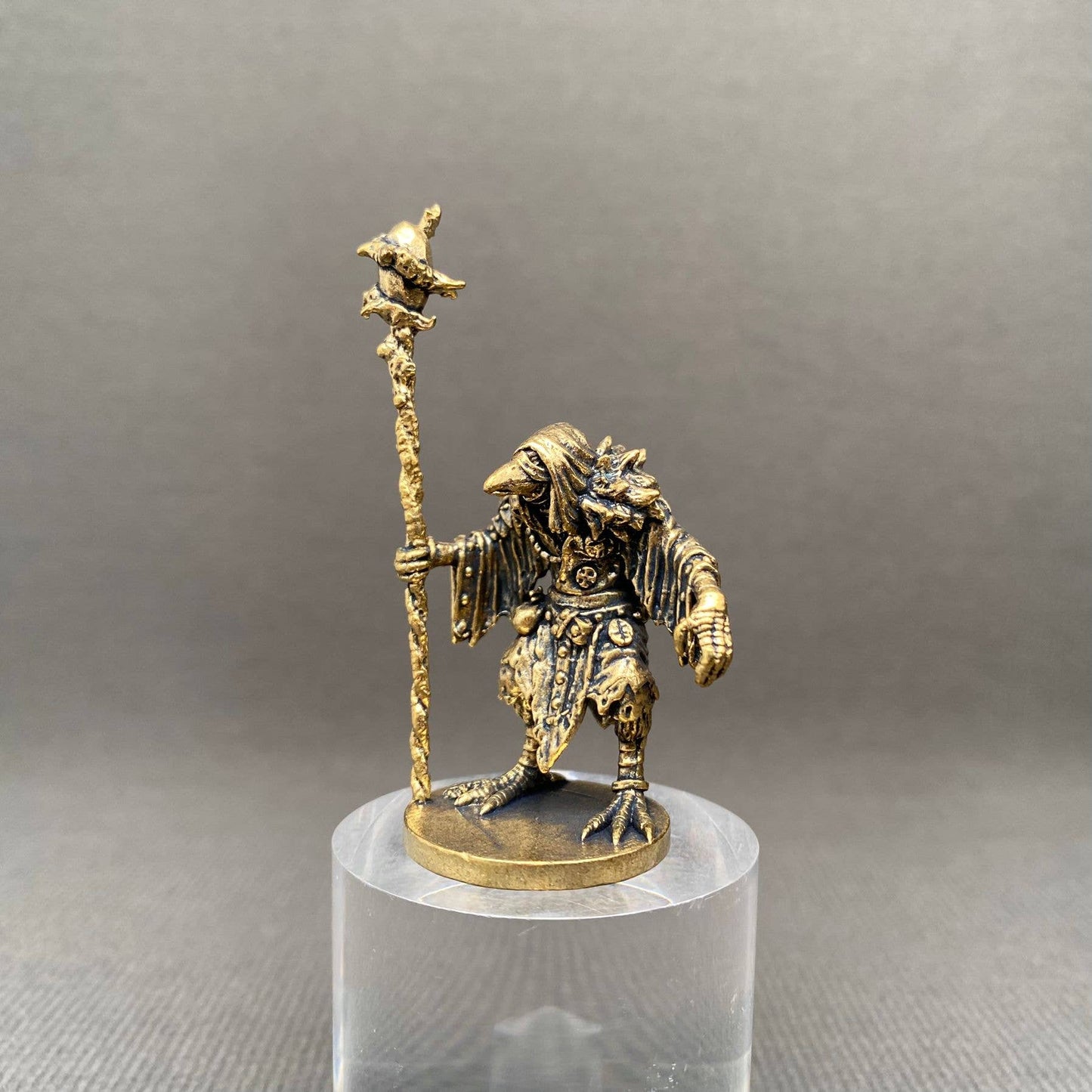 Brass figurine of a birdman warrior with a staff on a clear stand against a gray background
