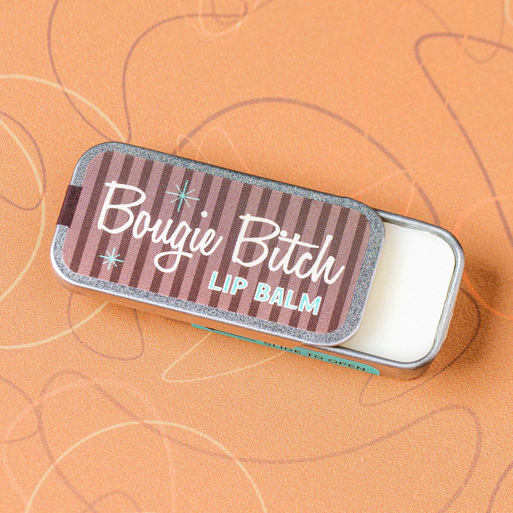 Lip balm tin with 'Bougie Bitch' text on a textured orange background