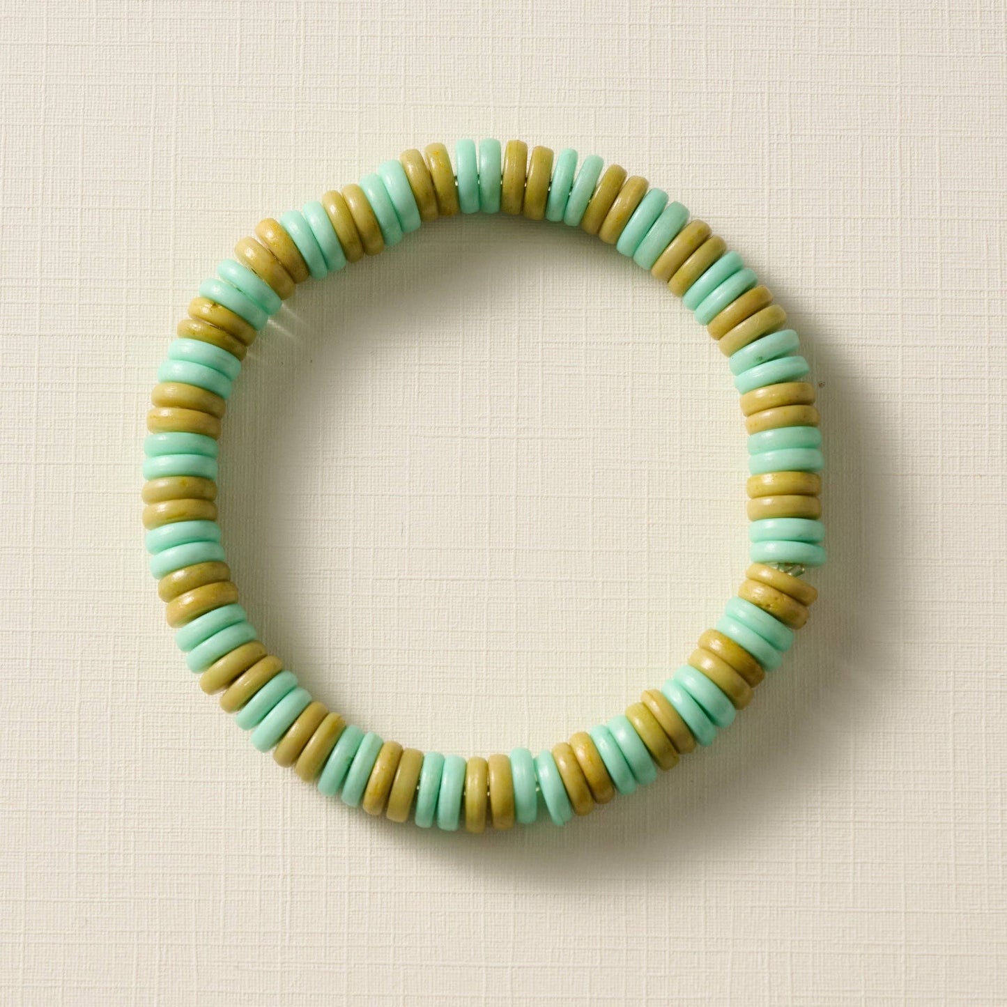 Beaded bracelet with green and olive beads on a beige background