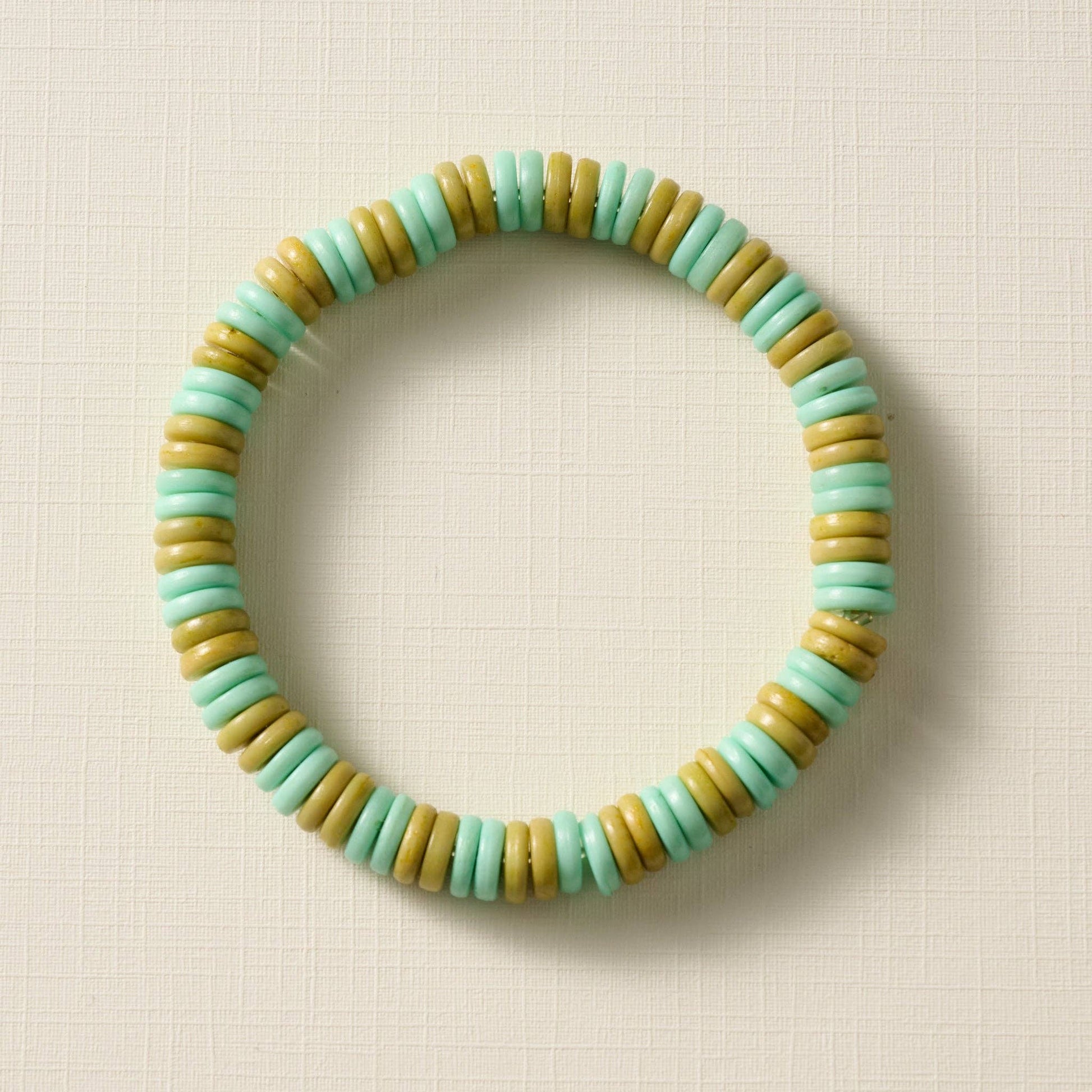 Beaded bracelet with green and olive beads on a beige background