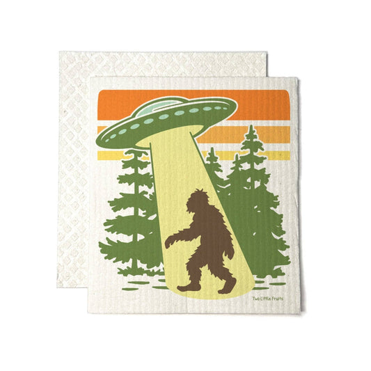 Swedish Dishcloth with a design of a UFO over a forest with a Bigfoot silhouette, on a white background.