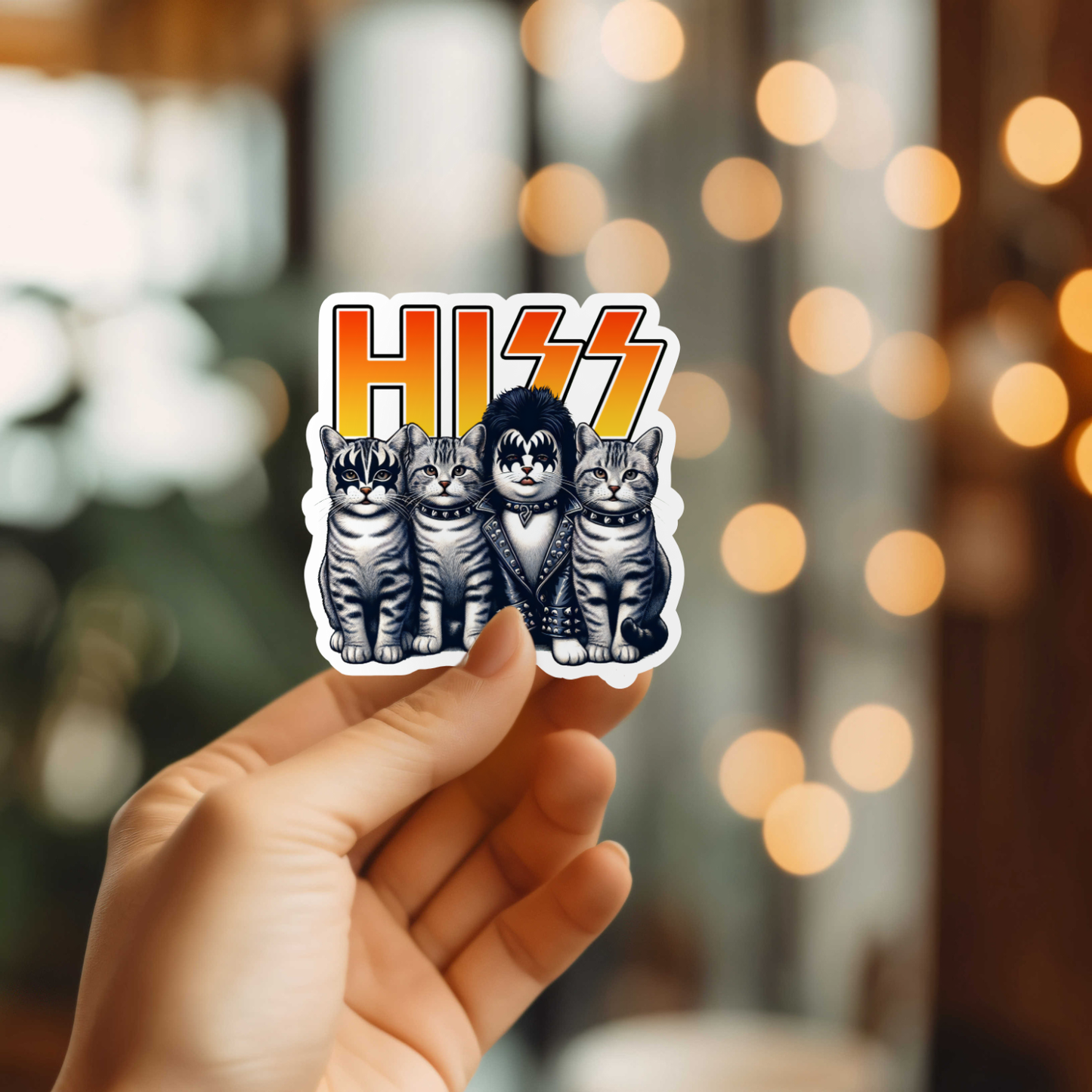 Sticker with 'HISS' design featuring cats held by a hand against a blurred background.