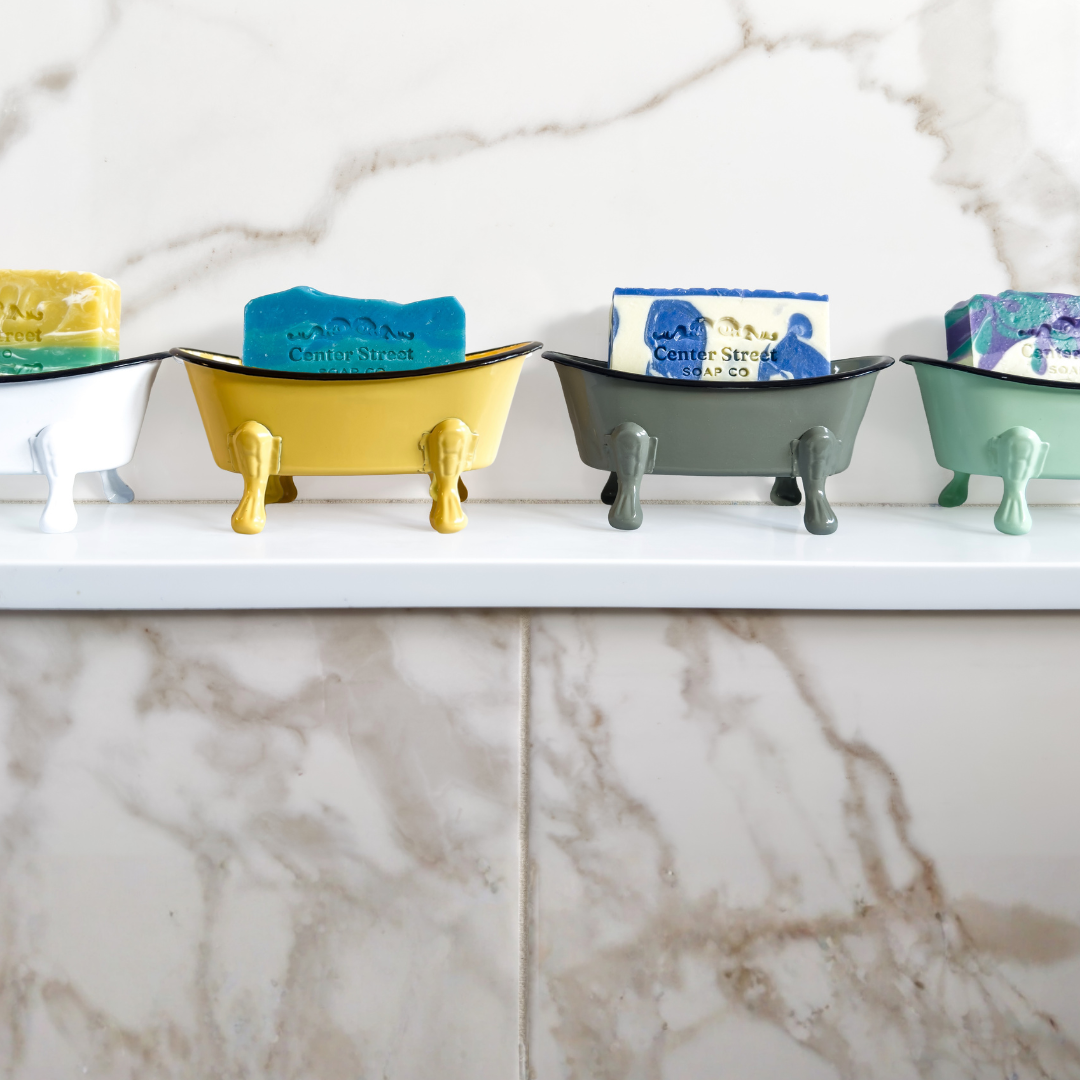 Colorful soap holders shaped like bathtubs on a marble countertop.