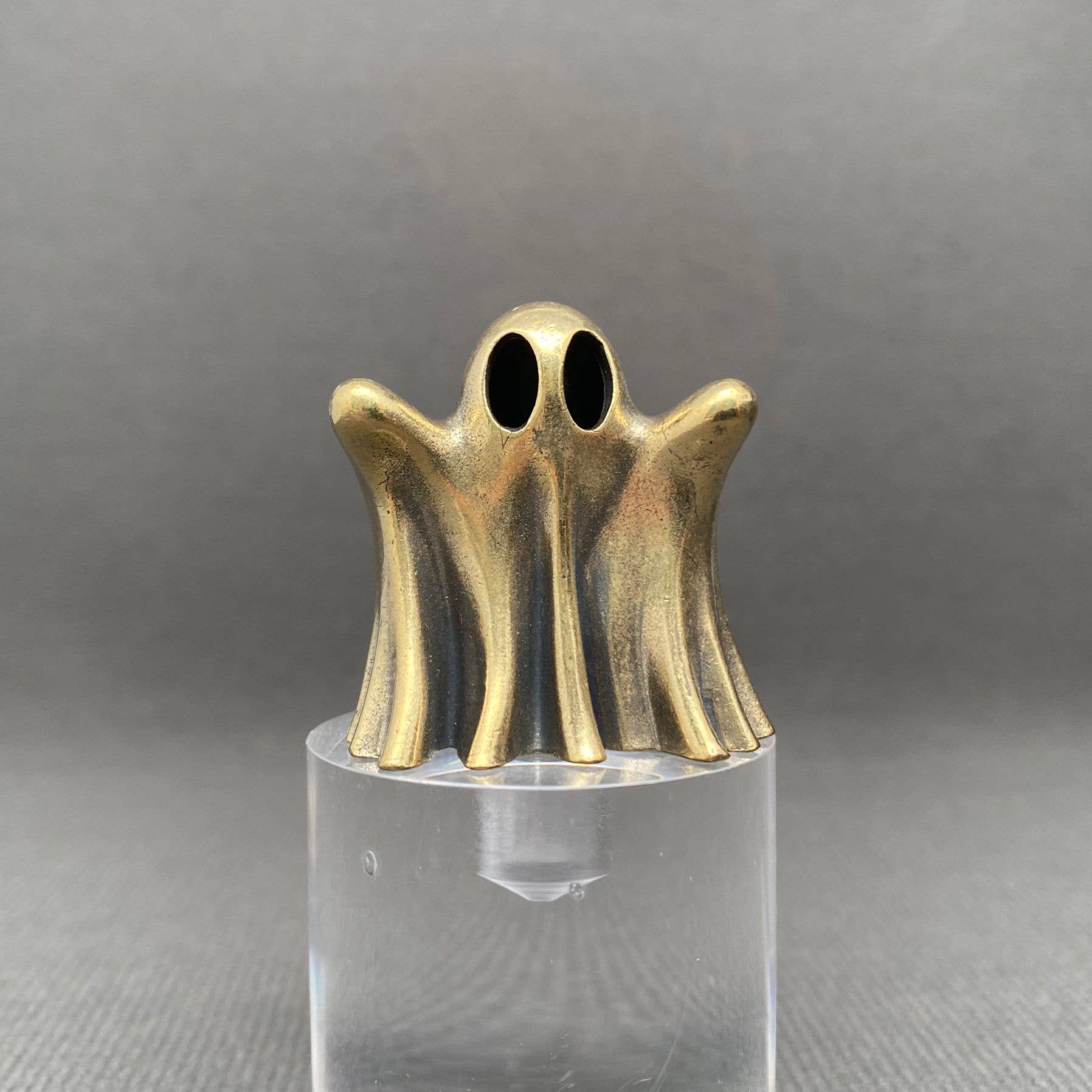 Brass figurine ghost on a clear stand against a gray background
