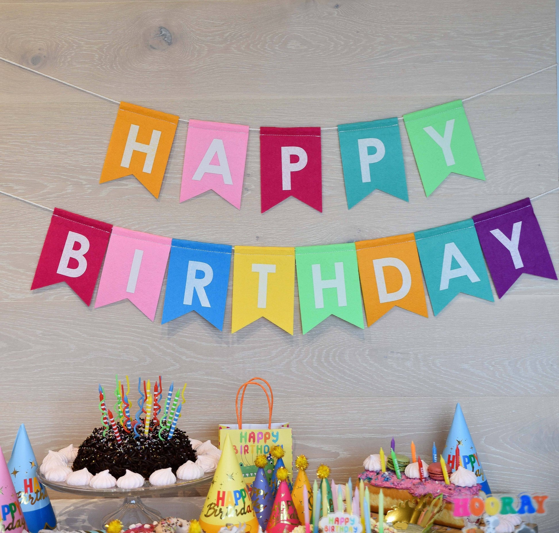 Colorful felt 'Happy Birthday' banner with birthday cake and decorations on a wooden surface.