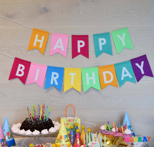 Colorful felt 'Happy Birthday' banner with birthday cake and decorations on a wooden surface.