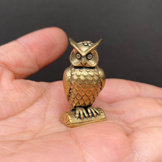 Small brass owl figurine held in a hand against a dark background