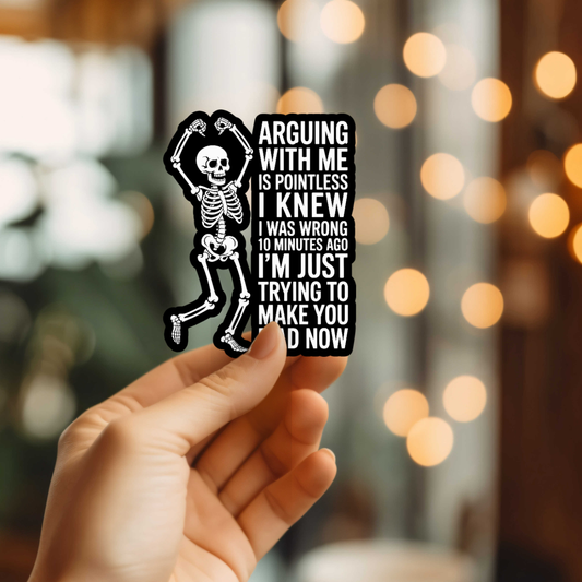 Hand holding a sticker with a skeleton design and text against a blurred background with lights.