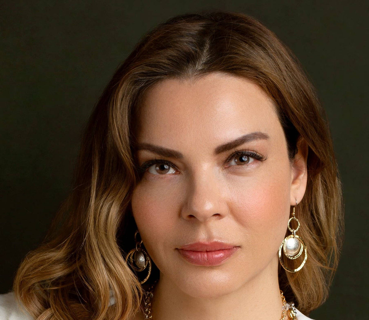 Woman wearing gold earrings with a dark background