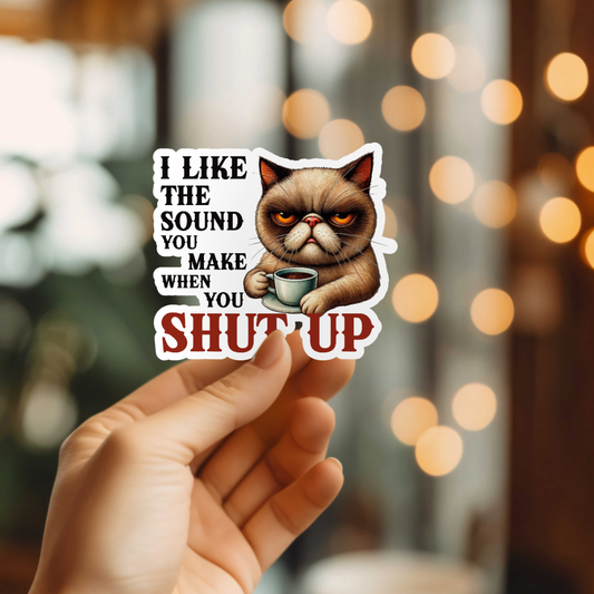 Sticker with a cat holding a coffee cup and text held by a hand against a blurred background