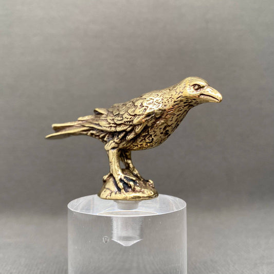 Brass figurine Raven on a clear stand against a gray background