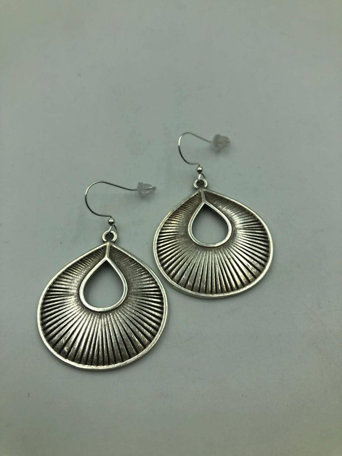 A pair of silver-toned teardrop dangle earrings with a textured sunburst or ribbed pattern, displayed on a neutral gray background.