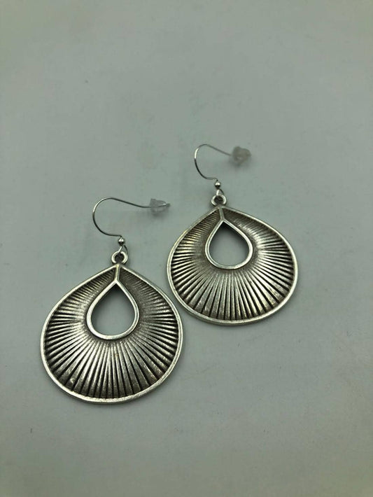 A pair of silver-toned teardrop dangle earrings with a textured sunburst or ribbed pattern, displayed on a neutral gray background.