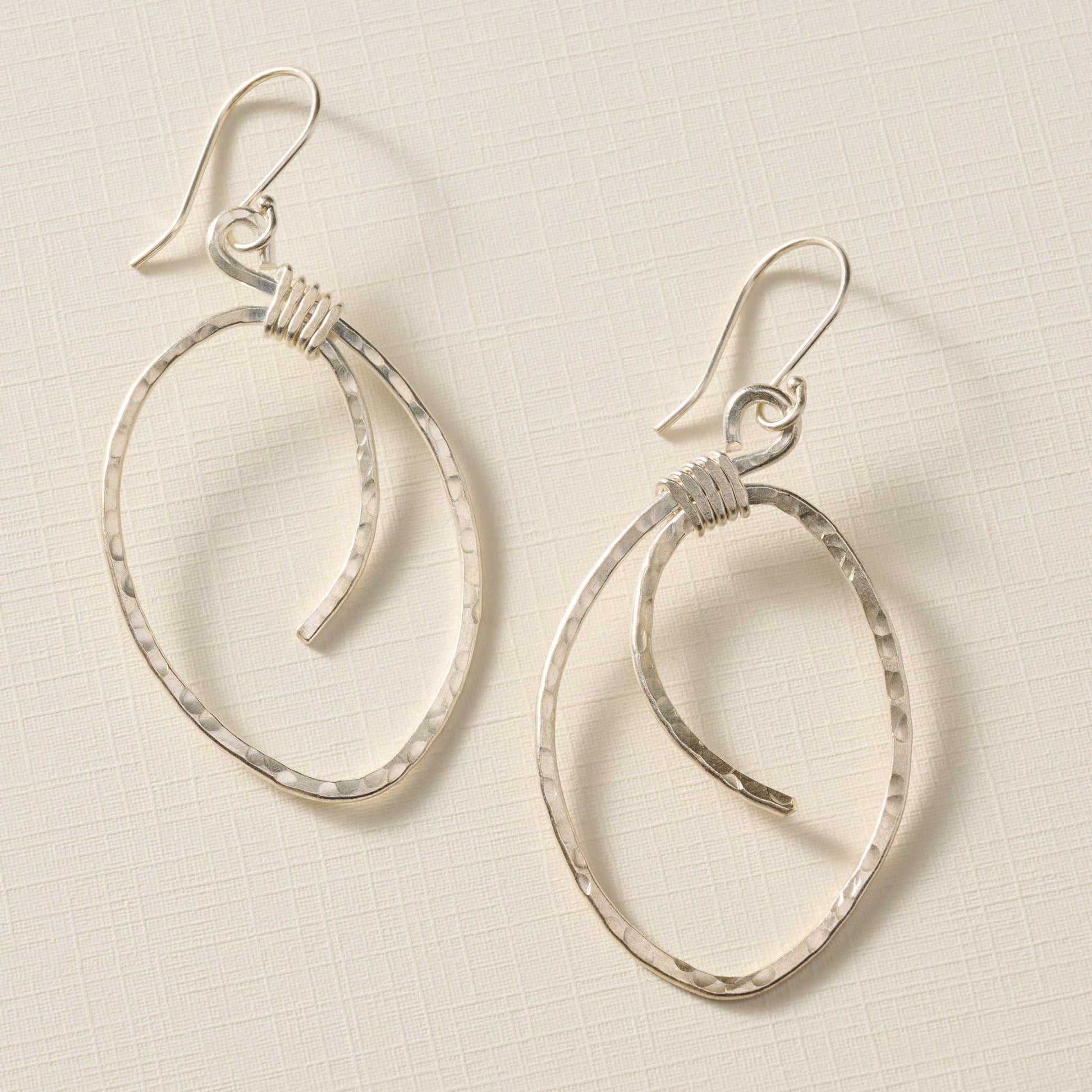 Pair of silver hoop earrings on a textured beige background