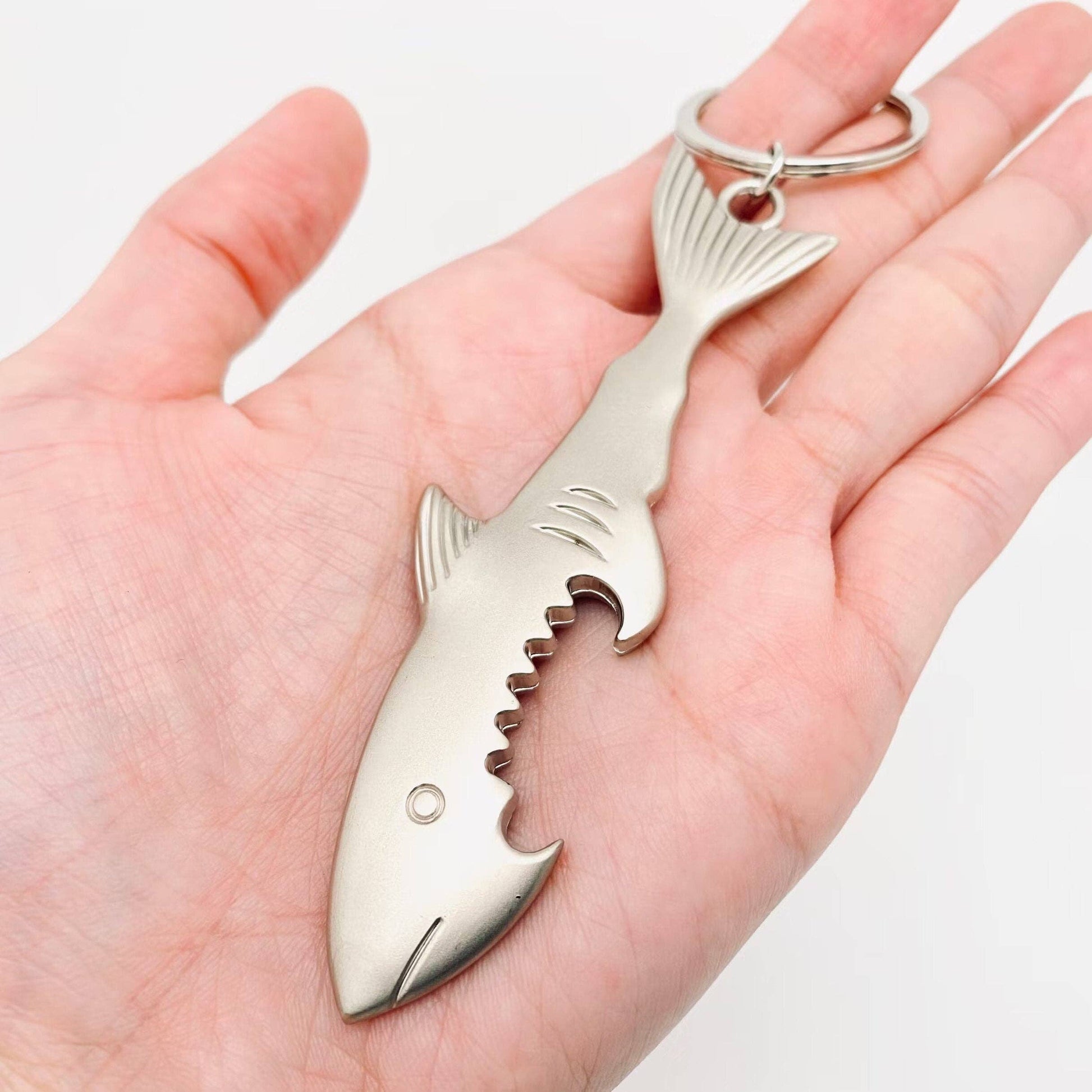 Shark-shaped bottle opener keychain held in a hand against a white background