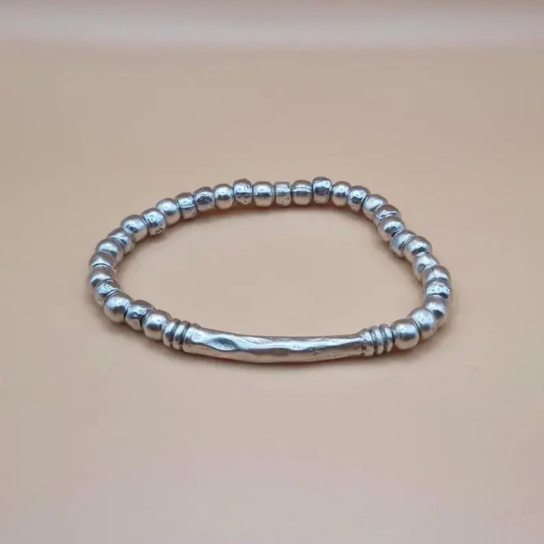 A sterling silver beaded bracelet with a textured central bar, displayed on a solid beige background.
