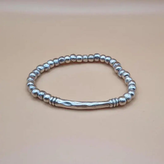 A sterling silver beaded bracelet with a textured central bar, displayed on a solid beige background.