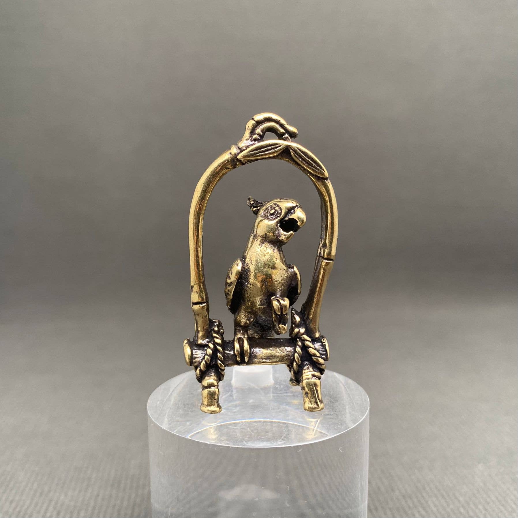 Brass parrot sculpture on a stand with a gray background