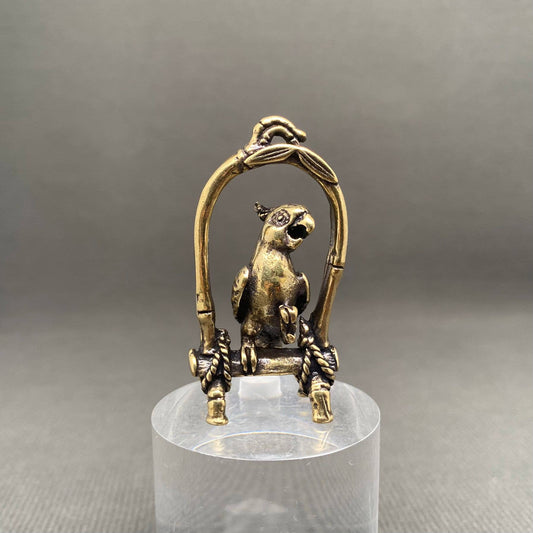 Brass parrot sculpture on a stand with a gray background