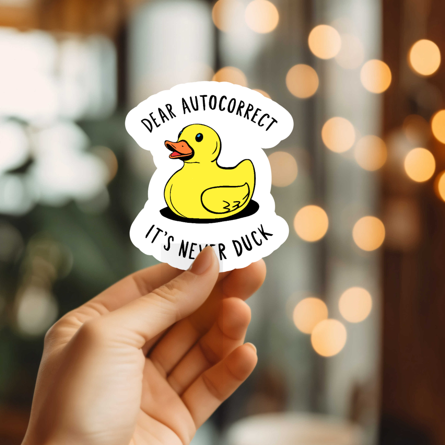 Hand holding a sticker with a duck graphic and text against a blurred background