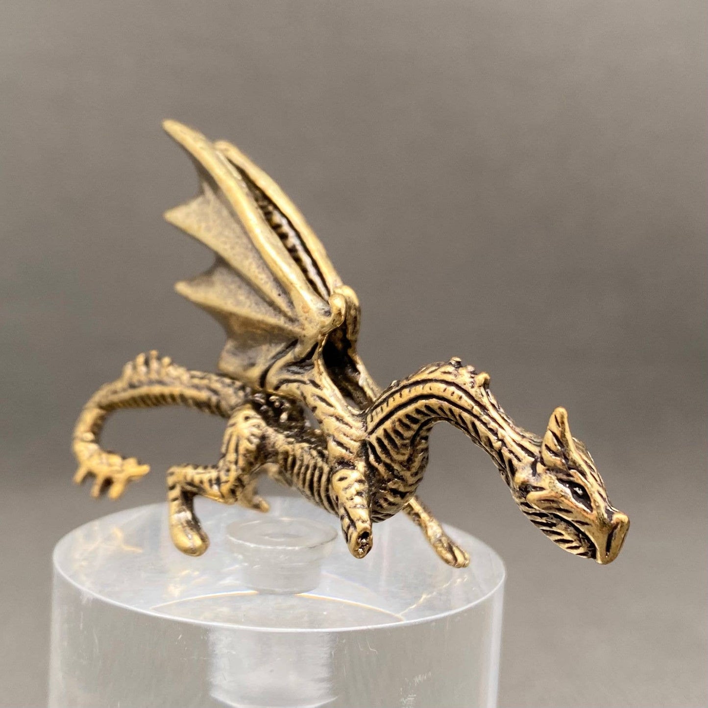 Brass figurine dragon on a clear stand with a gray background