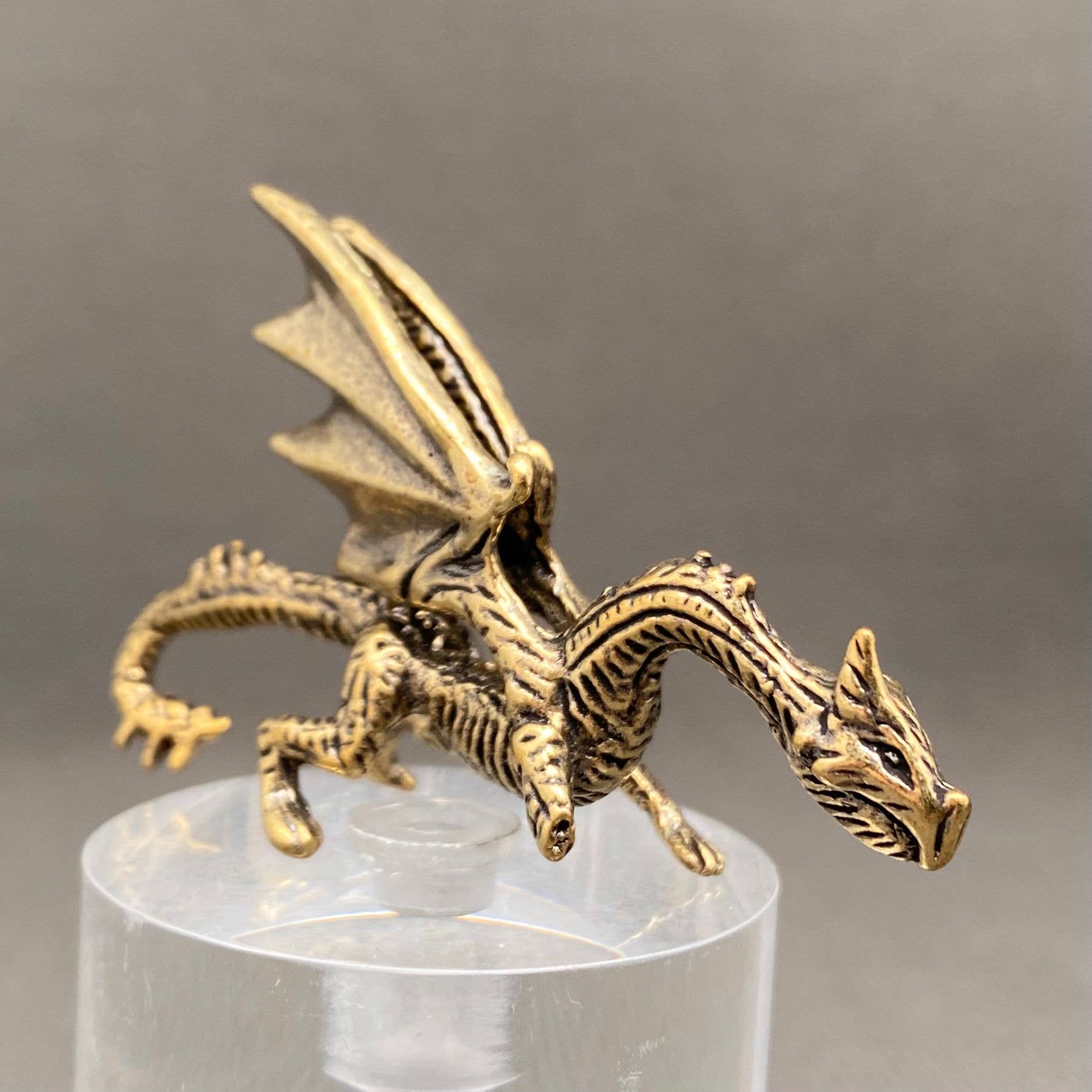 Brass figurine dragon on a clear stand with a gray background