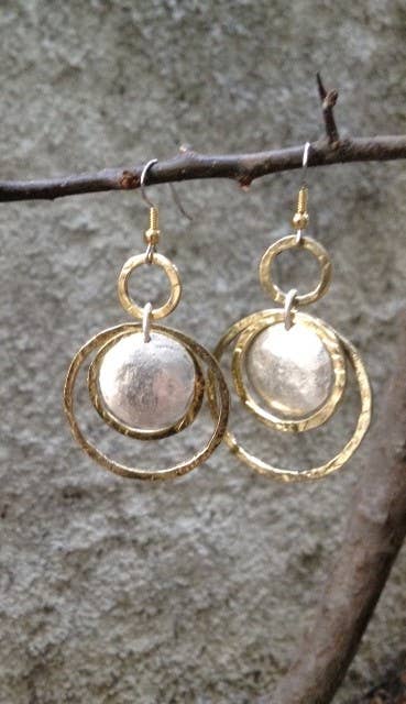 Gold and silver earrings hanging on a branch against a stone wall background