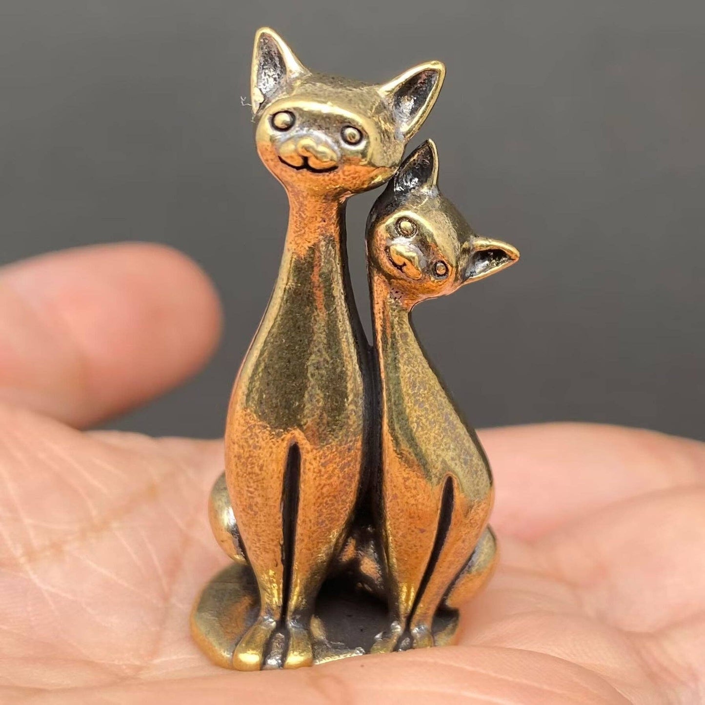 Brass figurine cats held in a hand against a dark background