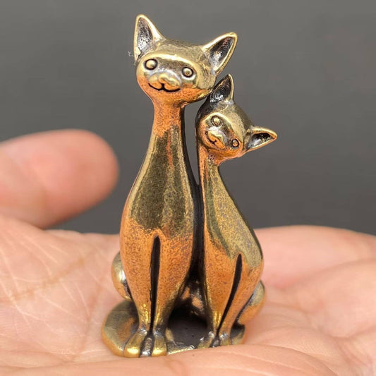 Brass figurine cats held in a hand against a dark background