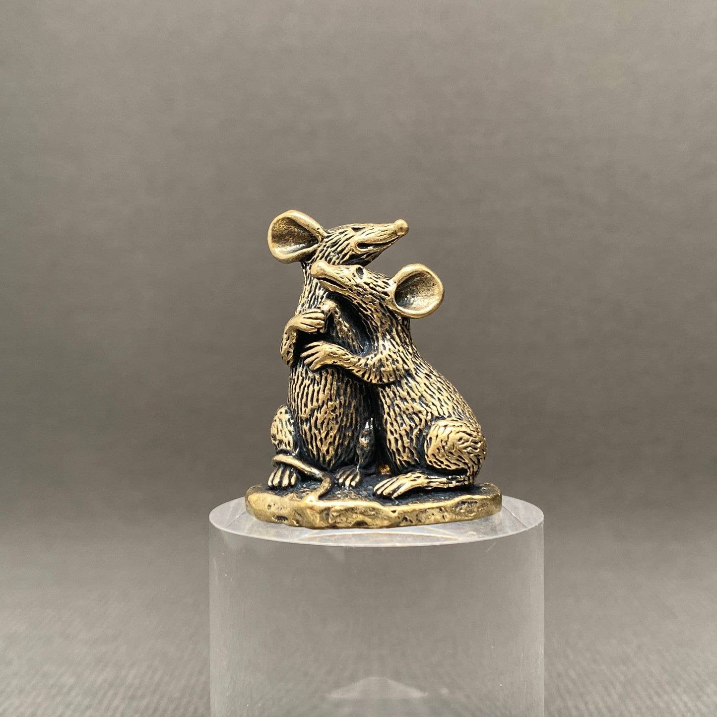 Brass pair of mice figurine on a clear pedestal against a gray background