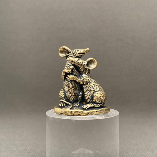 Brass pair of mice figurine on a clear pedestal against a gray background