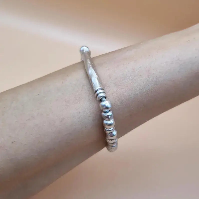 A textured sterling silver beaded bangle bracelet worn on a person's wrist, shown against a soft beige background.
