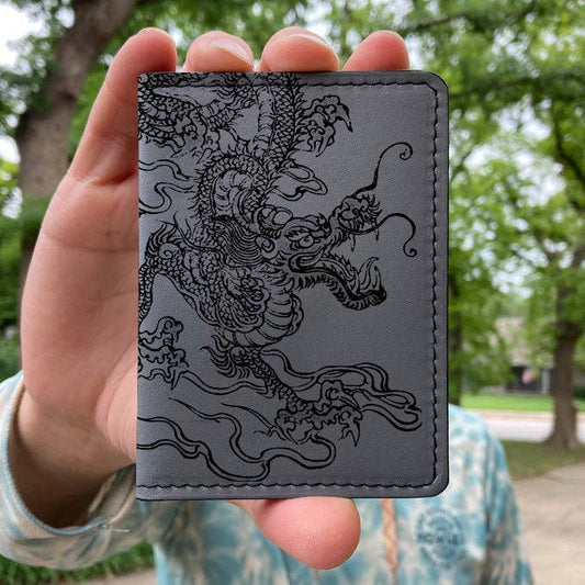 Person holding a gray wallet with a black dragon design outdoors