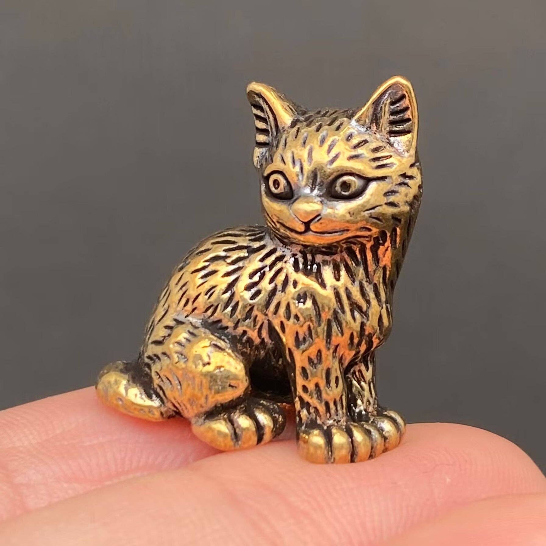 Brass figurine cat held in a hand against a dark background