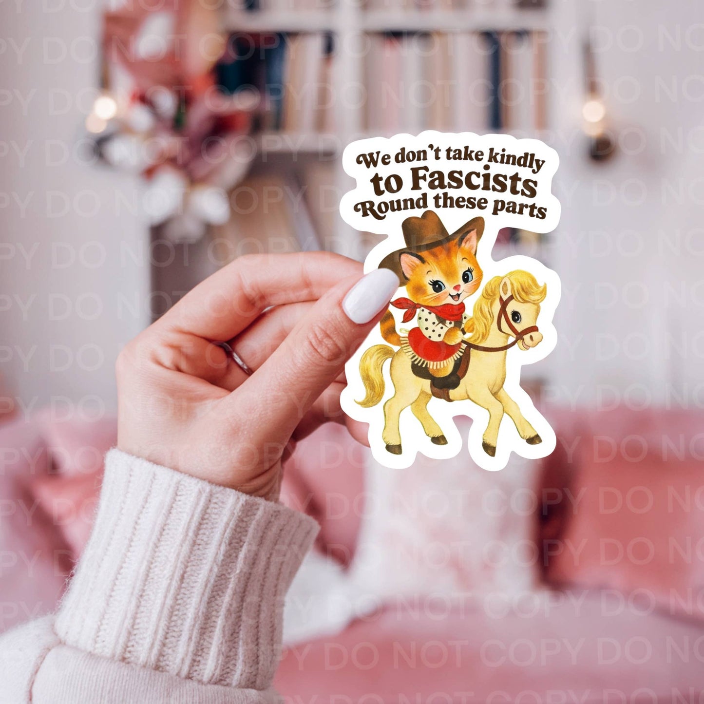 Hand holding a sticker with cartoon cat on a horse and text "We don't take kindly to Fascists round these parts"