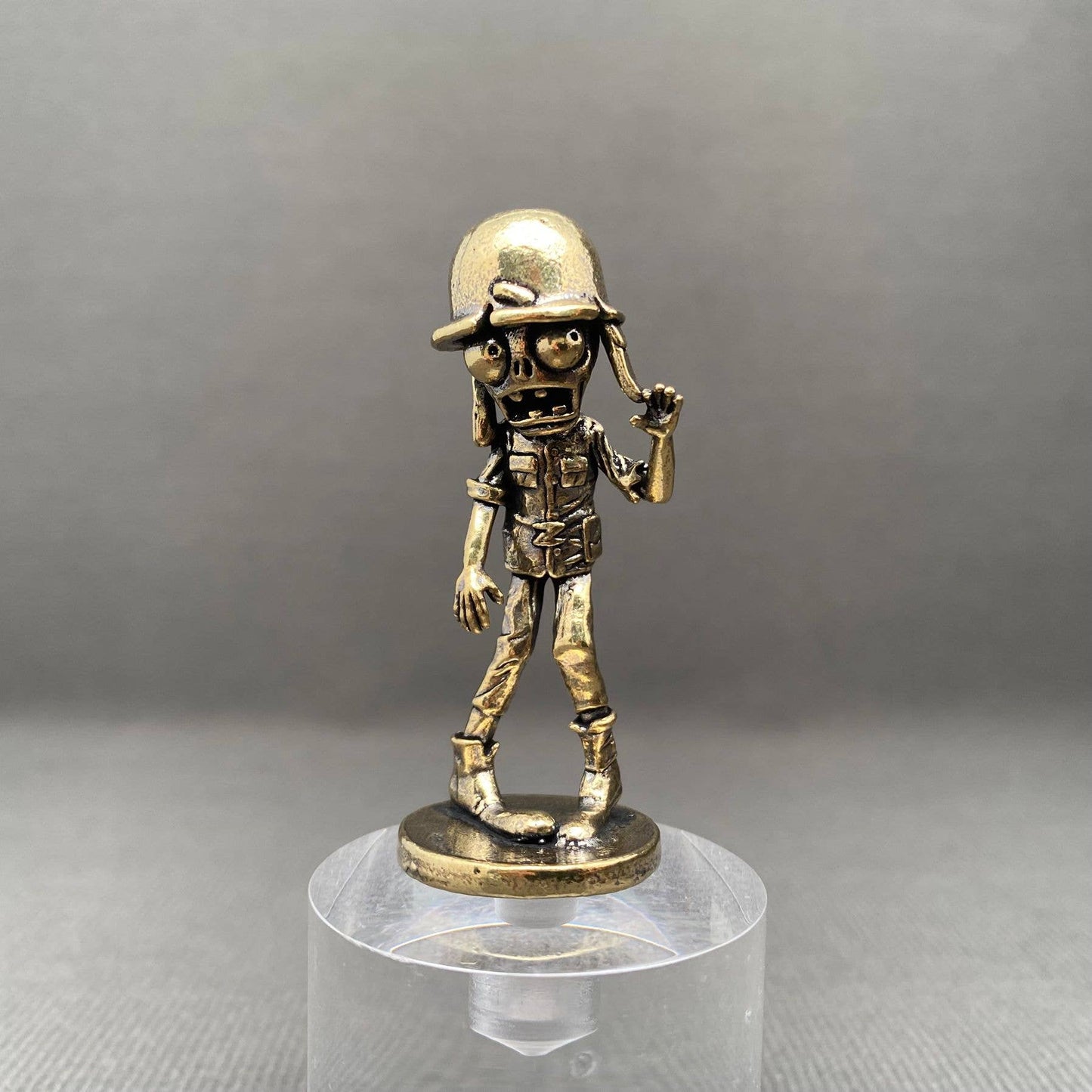 Bronze figurine of a zombie soldier on a clear stand against a gray background