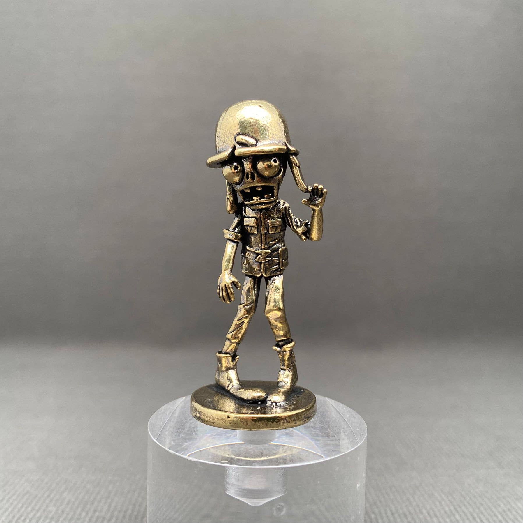 Bronze figurine of a zombie soldier on a clear stand against a gray background