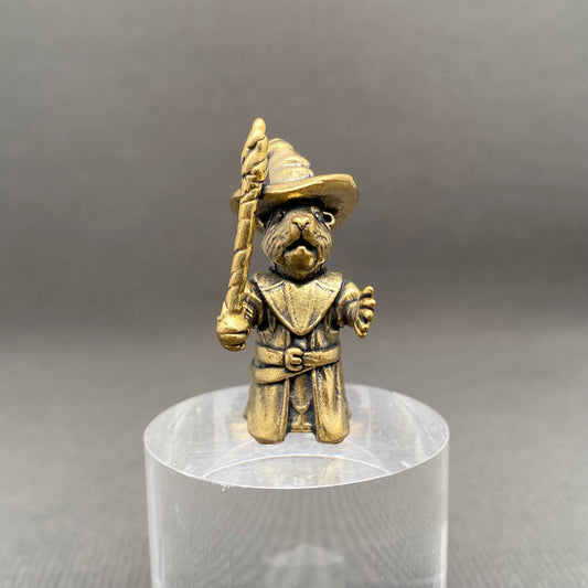 Brass figurine of a dog in a wizard costume holding a wand on a clear stand against a gray background