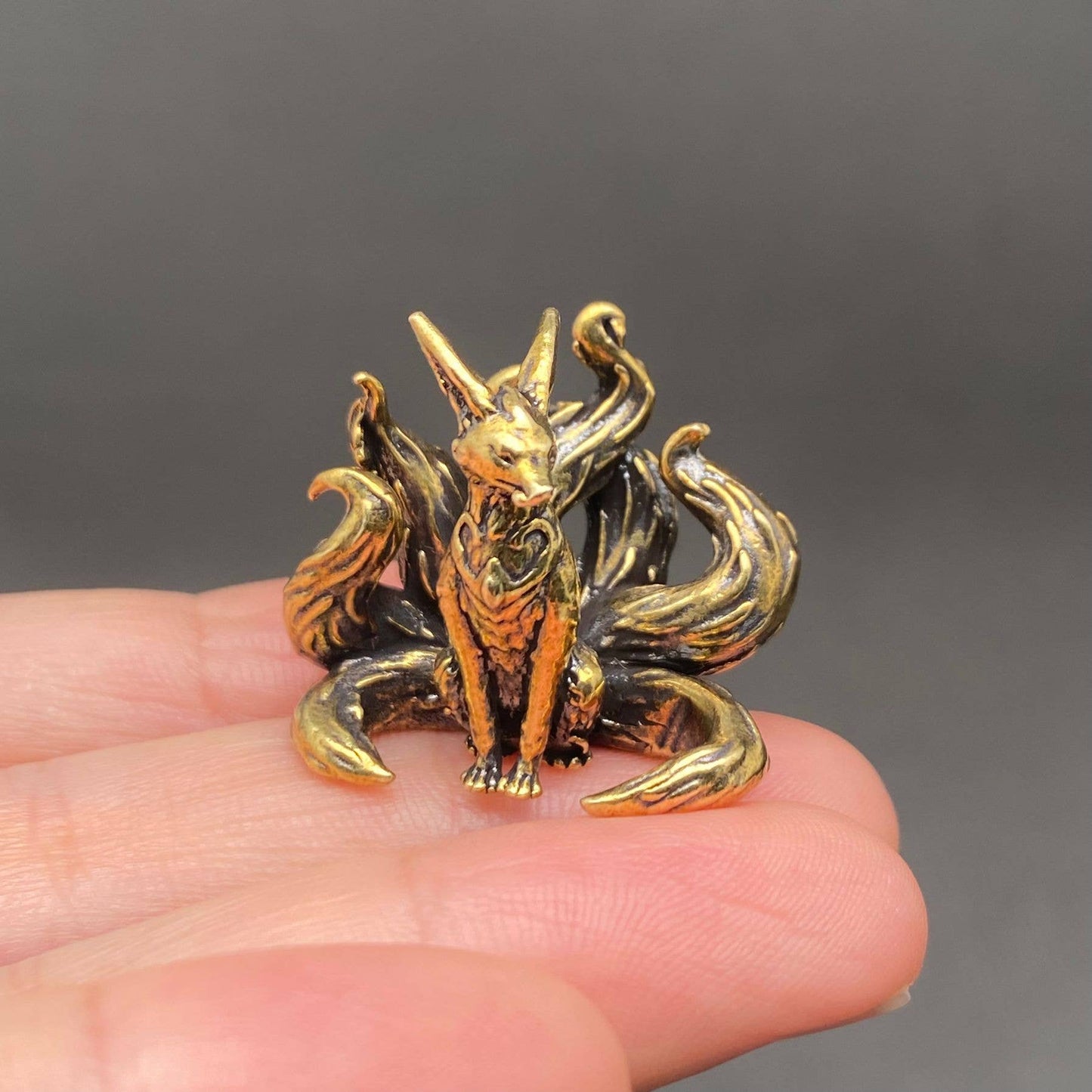 Brass 7 tails fox figurine held in a hand against a dark background
