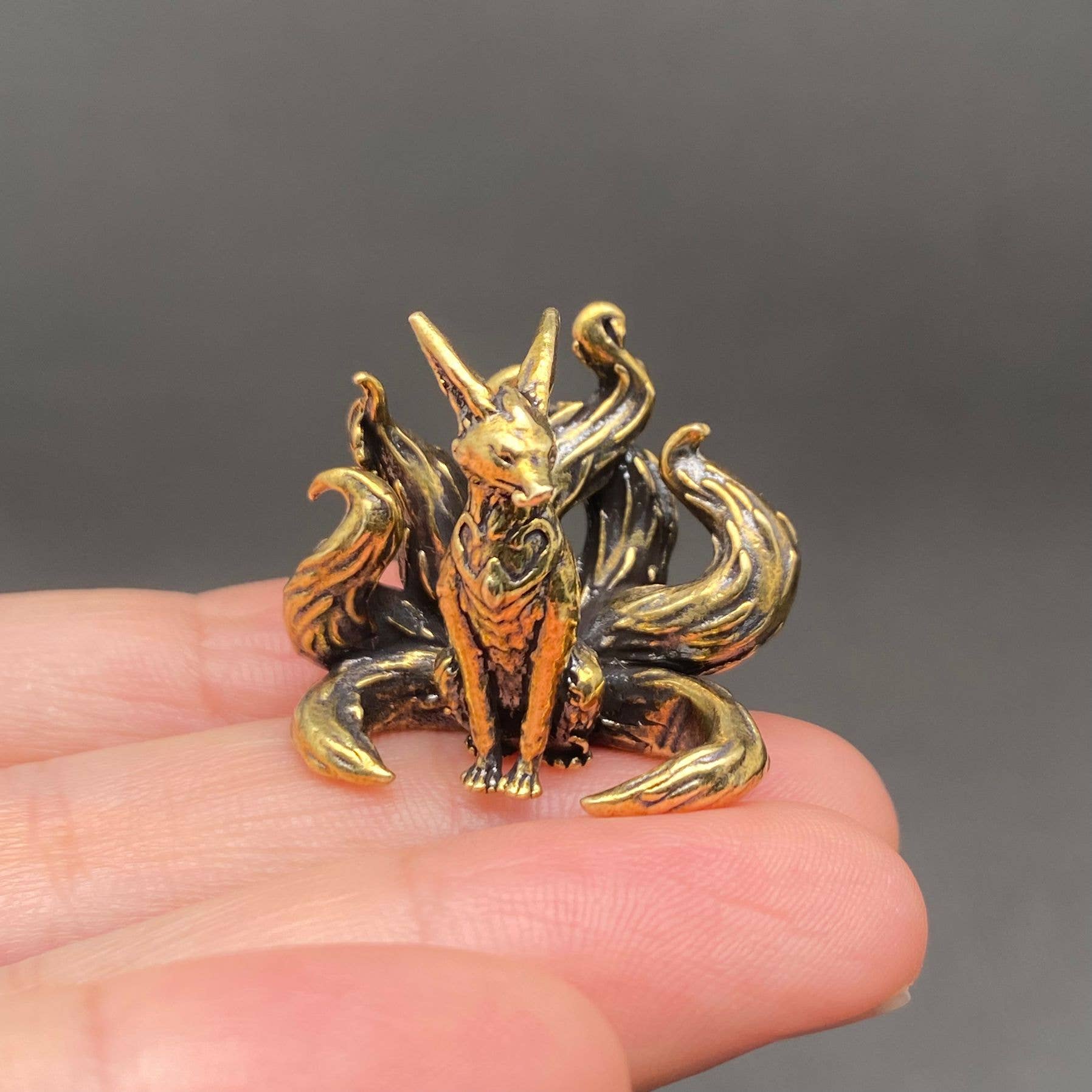 Brass 7 tails fox figurine held in a hand against a dark background