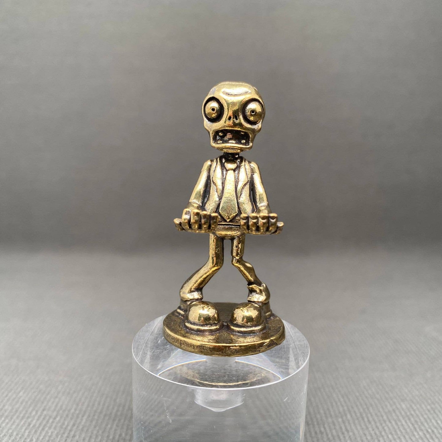 Brass figurine of a Zombie character on a clear stand against a gray background