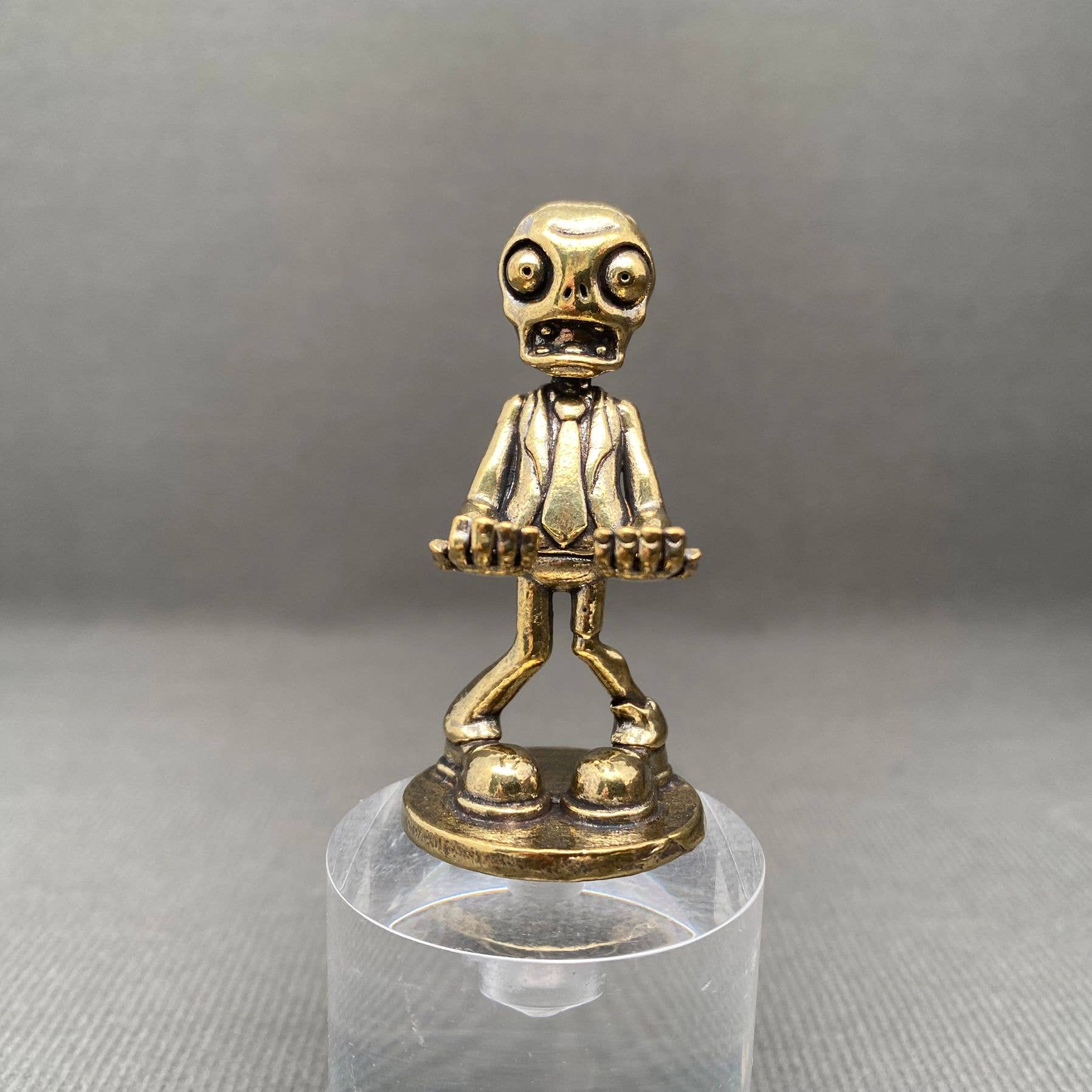 Brass figurine of a Zombie character on a clear stand against a gray background