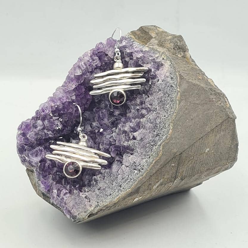 Silver earrings with gemstones on a purple crystal rock