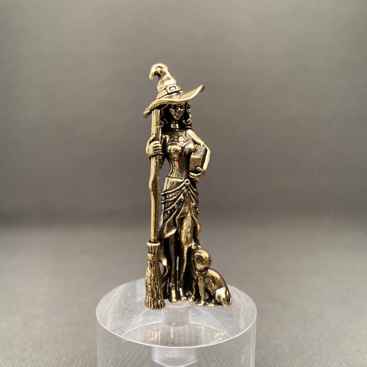 Brass figurine of a witch with a broomstick and a dog on a clear stand against a gray background